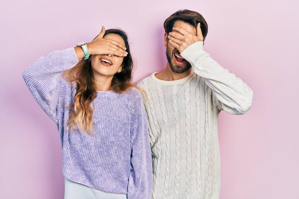 Jeune couple hispanique portant des vêtements décontractés souriant et riant avec la main sur le visage couvrant les yeux pour la surprise. concept aveugle.  - Photo, image