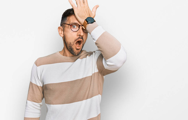 Handsome man with beard wearing casual clothes and glasses surprised with hand on head for mistake, remember error. forgot, bad memory concept.  - Photo, Image