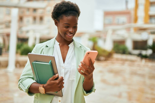 Genç Afrikalı Amerikalı iş kadını şehirde akıllı telefon kullanarak mutlu bir şekilde gülümsüyor.. - Fotoğraf, Görsel