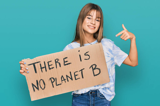 tiener Kaukasisch meisje houden er is geen planeet b banner glimlachen gelukkig wijzend met hand en vinger  - Foto, afbeelding