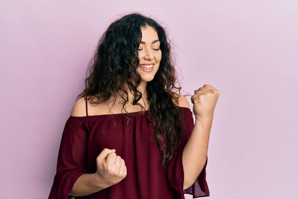 Young brunette woman with curly hair wearing casual clothes celebrating surprised and amazed for success with arms raised and eyes closed  - Photo, Image