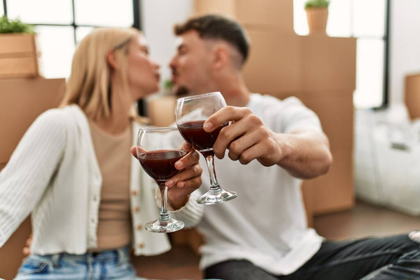 Young caucasian couple toasting with red wine glass sitting at new home. - Fotó, kép