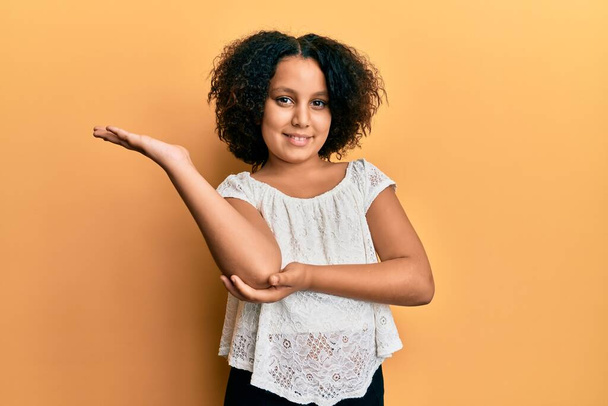 Young little girl with afro hair wearing casual clothes smiling cheerful presenting and pointing with palm of hand looking at the camera.  - Фото, зображення
