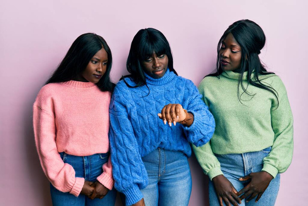 Tre giovani amici afroamericani che indossano maglione invernale in lana controllano il tempo sull'orologio da polso, rilassati e fiduciosi  - Foto, immagini