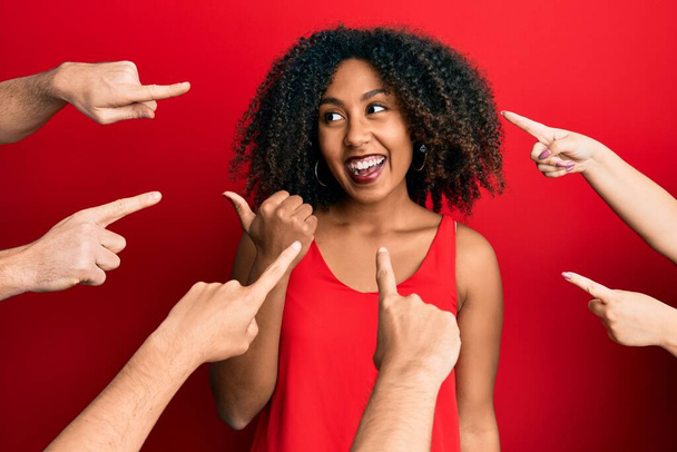 Afro saçlı, güzel Afro-Amerikalı kadın etrafta parmaklarını göstererek baş parmağını yana kaldırıyor ve ağzı açık gülümsüyor.  - Fotoğraf, Görsel