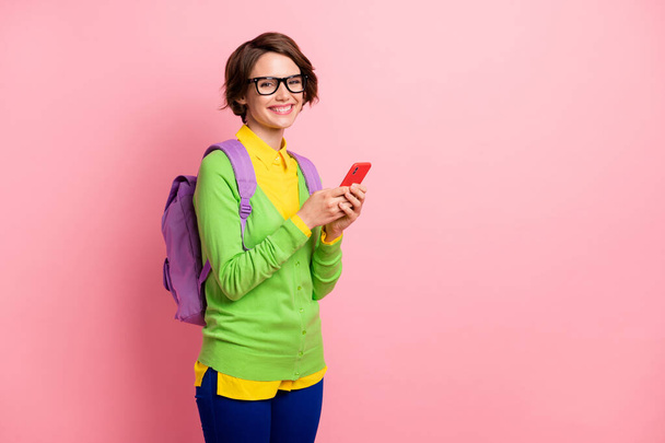Photo of cute young lady dressed yellow shirt glasses backpack holding modern device empty space isolated pink color background - Foto, immagini