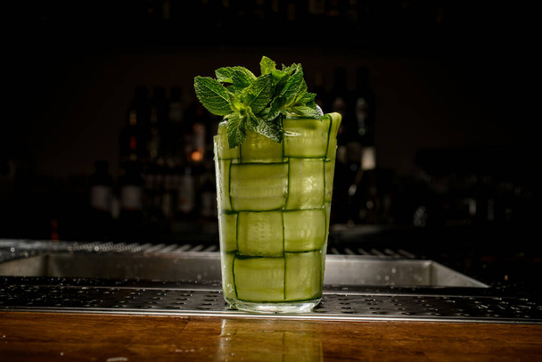 front view of glass with cocktail garnished with mint and slices of fresh cucumber - Фото, изображение