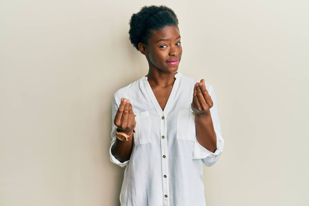 Chica afroamericana joven con ropa casual haciendo gesto de dinero con las manos, pidiendo pago de sueldo, negocio millonario  - Foto, imagen
