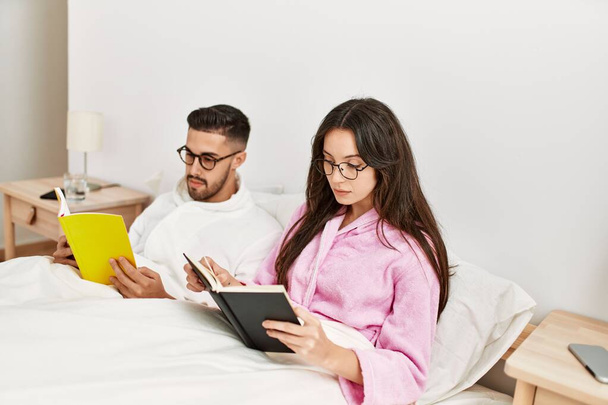 Junges hispanisches Paar liest Buch zu Hause im Bett liegend. - Foto, Bild