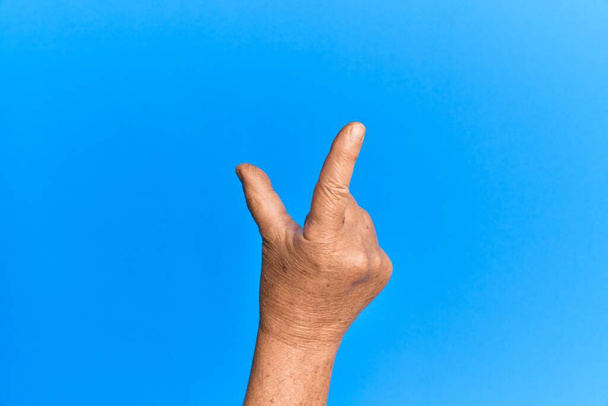 Käsi vanhempi latino mies yli sininen eristetty tausta poiminta ja ottaen näkymätön asia, pitämällä esine sormin näyttää tilaa  - Valokuva, kuva