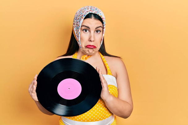 Young hispanic woman wearing pin up style holding vinyl disc depressed and worry for distress, crying angry and afraid. sad expression.  - Photo, Image