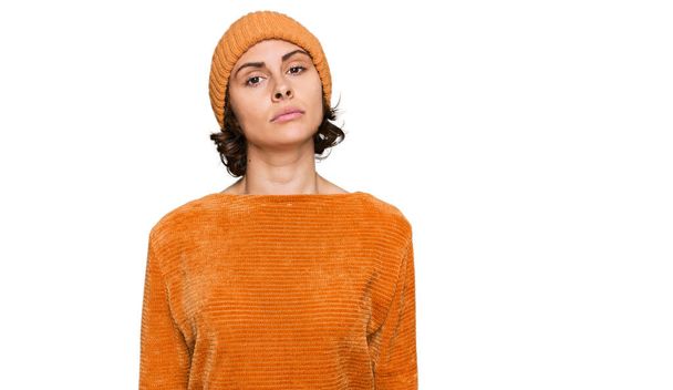 Mujer hispana joven con ropa casual y gorra de lana relajada con expresión seria en la cara. simple y natural mirando a la cámara.  - Foto, imagen