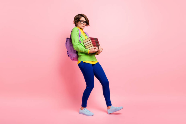 Full length photo of young woman wear green cardigan spectacles rucksack walking afraid fall stack book isolated pink color background - Foto, afbeelding