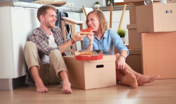 Nuori pari pitää pizzalounastauon lattialla muutettuaan uuteen kotiin laatikot ympärillään. Nuori pari - Valokuva, kuva