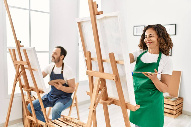 Dos estudiantes de mediana edad sonriendo feliz pintura en el estudio de arte. - Foto, Imagen