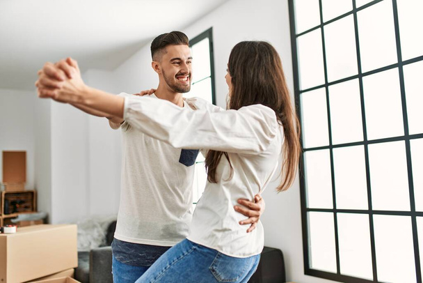 Joven pareja hispana sonriendo feliz bailando en nuevo hogar. - Foto, imagen