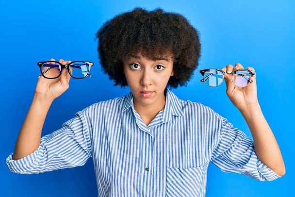 Νεαρή Ισπανίδα που κρατάει γυαλιά σκεπτική και νευρική, συνοφρυωμένη από το πρόβλημα. αρνητικό πρόσωπο.  - Φωτογραφία, εικόνα