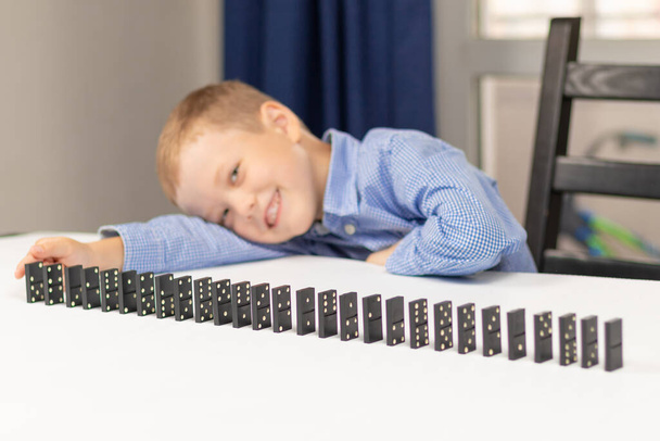 Sei anni ragazzo carino gioca a domino a casa su un tavolo di legno bianco. Concentrazione selettiva. Primo piano - Foto, immagini