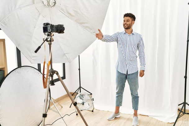 Arabischer junger Mann posiert als Model im Fotostudio und lächelt fröhlich und bietet Palmhände an, die Hilfe und Akzeptanz gibt.  - Foto, Bild