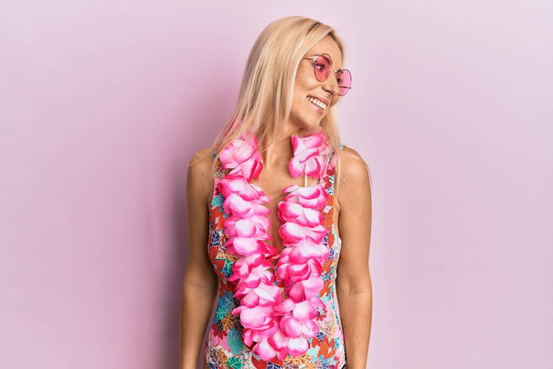 Young blonde woman wearing swimsuit and hawaiian lei looking away to side with smile on face, natural expression. laughing confident.  - Fotó, kép