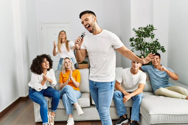 Skupina mladých přátel, kteří mají party zpěv píseň pomocí mikrofonu doma. - Fotografie, Obrázek