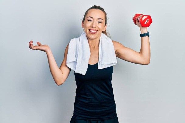 Young caucasian woman wearing sportswear using dumbbells screaming proud, celebrating victory and success very excited with raised arm  - Photo, Image