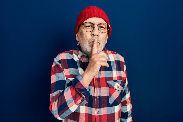 Knappe volwassen man draagt hipster look met wollen pet vragen om stil te zijn met de vinger op de lippen. stilte en geheim concept.  - Foto, afbeelding