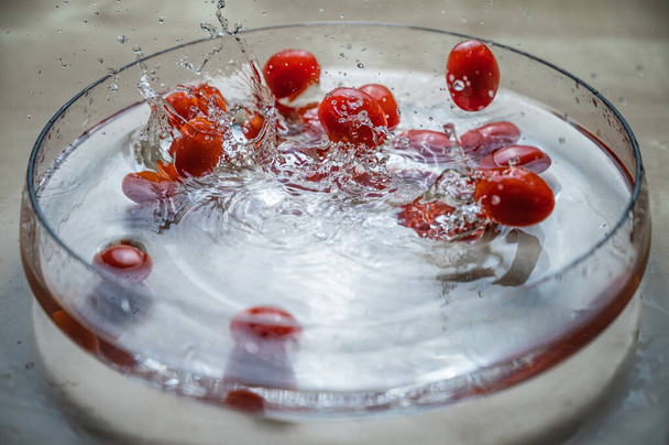 Antioxydant naturel végétal bio Groupe de tomates prunes cerises rouges fraîches (tomate bébé, tomate cerise) tombant sur le bol d'eau avec éclaboussure d'eau  - Photo, image