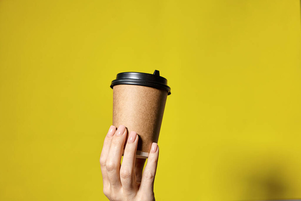 Hands holding two cups brown paper with black lid. Two coffee special offer or promo. Hands holding two cups on yellow screen background. Tea or Coffee to go. Brown paper cup with black lid. - Foto, Imagen