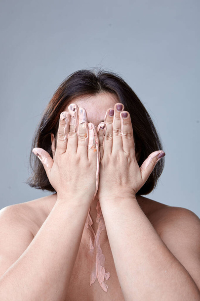 Η γυναίκα καλύπτει το πρόσωπό της με τα χέρια της. Δύο ανοιχτά χέρια με μπογιά καλύπτουν το πρόσωπο μιας γυναίκας. - Φωτογραφία, εικόνα