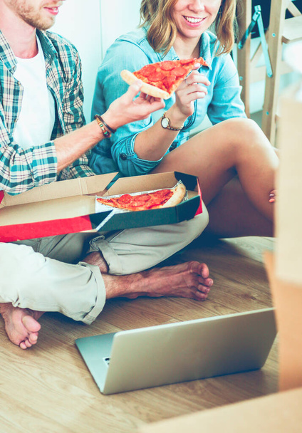 Young couple have a pizza lunch break on the floor after moving into a new home with boxes around them. Young couple - Fotoğraf, Görsel