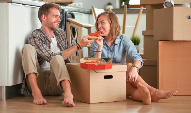 Young couple have a pizza lunch break on the floor after moving into a new home with boxes around them. Young couple - Fotó, kép