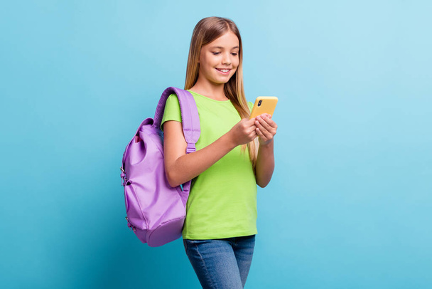 Photo of young smiling cheerful good mood positive girl browsing in internet wear violet rucksack isolated on blue color background - Foto, Imagen