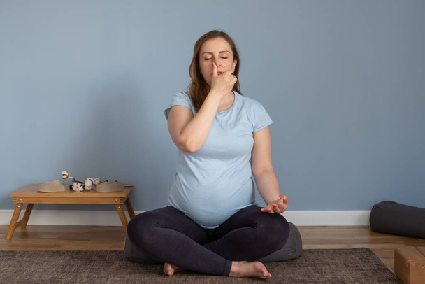Pregnant woman practices yoga at home breathing nadi shodhana pranayma - Photo, Image