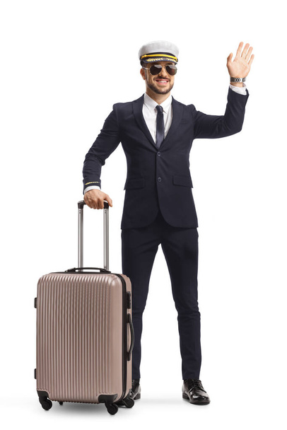 Full length portrait of a young pilot with a suitcase waving at camera isolated on white background - Fotoğraf, Görsel