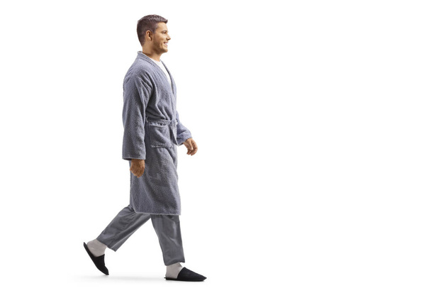 Full length profile shot of a young man wearing a robe and walking isolated on white background - Photo, image
