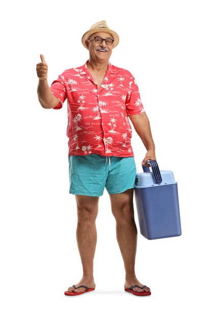 Mature male tourist holding a portable fridge and showing thumbs up isolated on white background - Zdjęcie, obraz