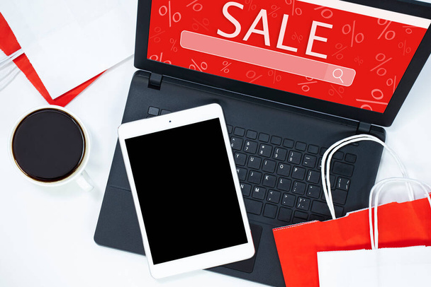 tablet, laptop, café e sacos de compras em um fundo leve. conceito de compras online - Foto, Imagem