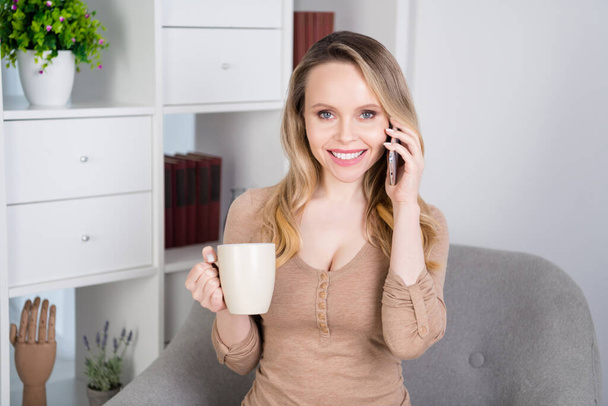 Photo of lovely sociable lady sit chair have telephone conversation drink cacao wear beige shirt in room indoors - Foto, Bild