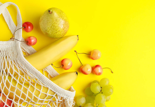 Eco-friendly cotton shopping bag. Ripe fruits in a mesh bag on a yellow background. Organic vegan food. Sustainable lifestyle and zero waste concept. - Photo, Image