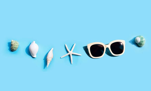 Sluneční brýle s hvězdicemi a exotickými mořskými lasturami na modré. Letní koncept pozadí - Fotografie, Obrázek