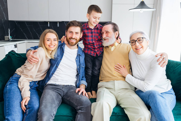 Mehrgenerationenfamilie sitzt zu Hause gemütlich auf Sofa und plaudert - Foto, Bild