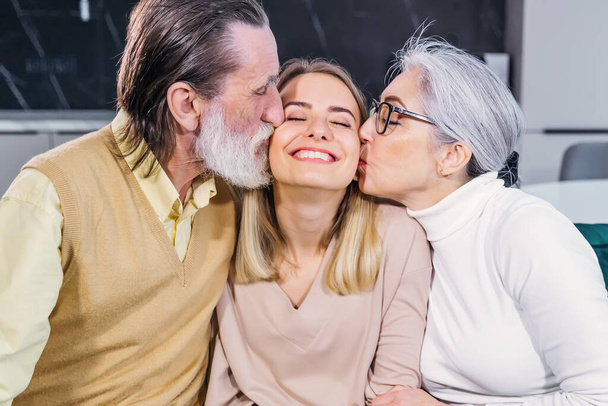 милая взрослая внучка и ее улыбающиеся пенсионеры пришли навестить красивых бабушку и дедушку, сидя на диване в гостиной на дому, наслаждаясь, проводить время вместе целовать девушку от радости - Фото, изображение