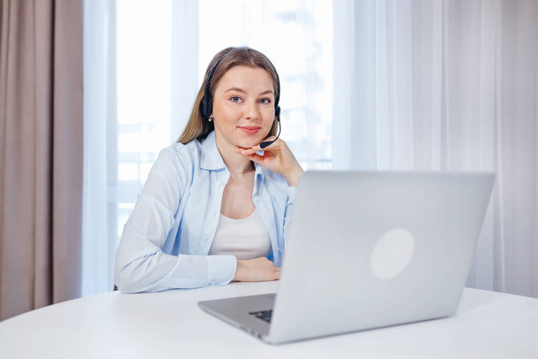 Młoda uśmiechnięta kobieta biznesu z piegami w słuchawkach komunikuje się przez połączenie wideo, laptop, konferencja online, zdalne biuro, - Zdjęcie, obraz