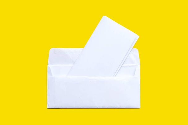Open witte envelop met papier op gele achtergrond. - Foto, afbeelding