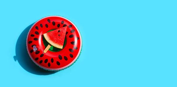 Watermelon slice popsicle on swim ring toy on blue background. Summer background concept - Foto, Imagen