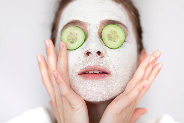 Краса жінки-домогосподарки з масками на обличчі і тримає огірок як поживні речовини для лікування її шкіри обличчя
 - Фото, зображення