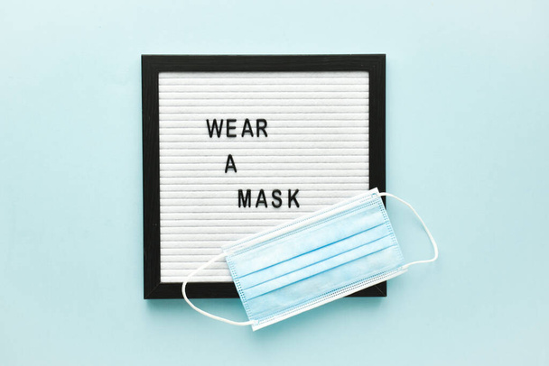 Un masque médical et un message texte sur un panneau de feutre sont mis sur le masque sur un fond bleu clair. - Photo, image