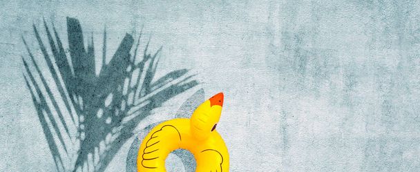 Tropikal palmiye yapraklı sarı ördek şişirilebilir beton arka planda gölge bırakır. Yaz arkaplanı kavramı - Fotoğraf, Görsel