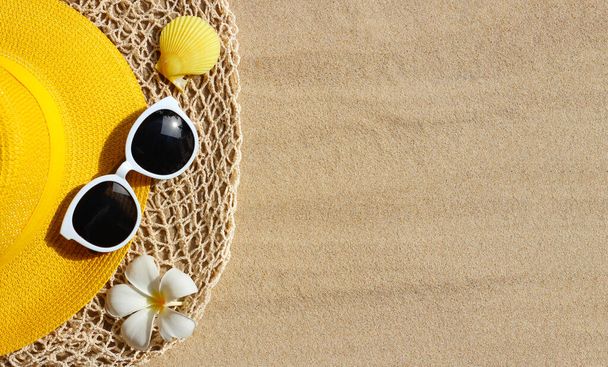  Yellow summer hat with sunglasses on sand. Top view - Photo, Image